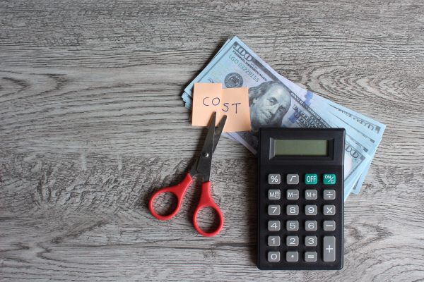 Scissor, calculator, money and note with text COST. Financial, cost cutting, reduce expenses concept